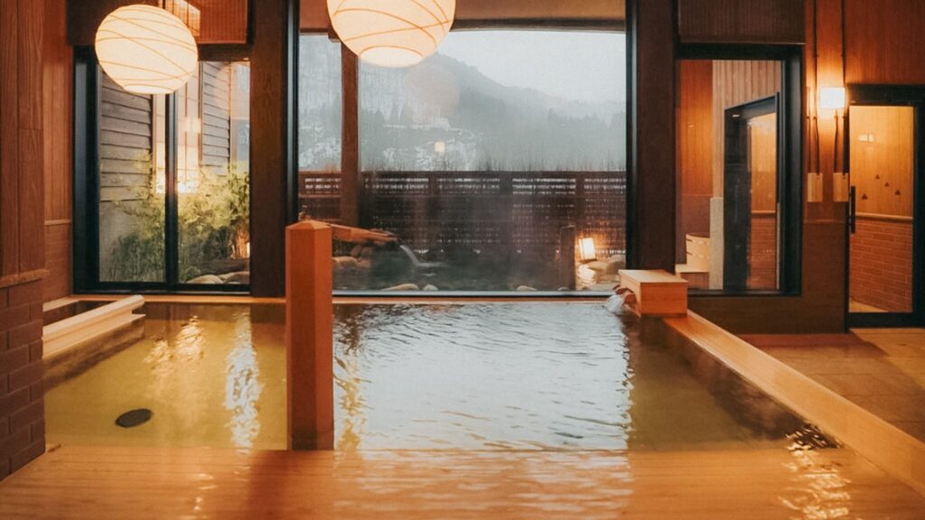 Pemandian air panas bergaya ryokan mewah dengan pencahayaan hangat dan pemandangan luar ruangan, pengalaman menginap eksklusif Private Trip Jepang