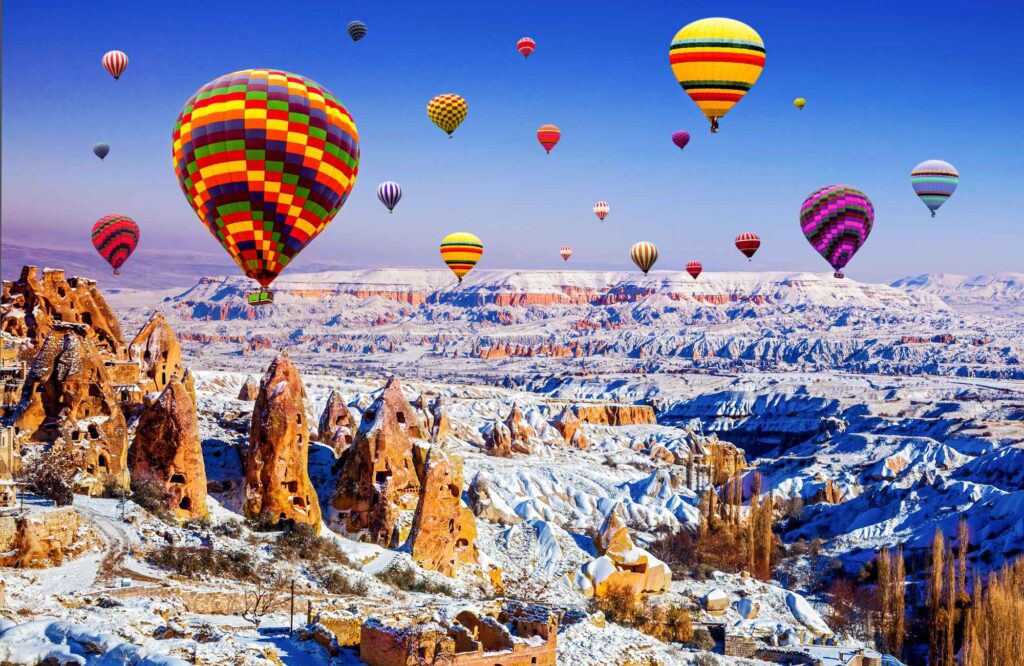 Pemandangan spektakuler balon udara di atas lembah bersalju Cappadocia, destinasi wajib untuk pengalaman liburan musim dingin di Turki