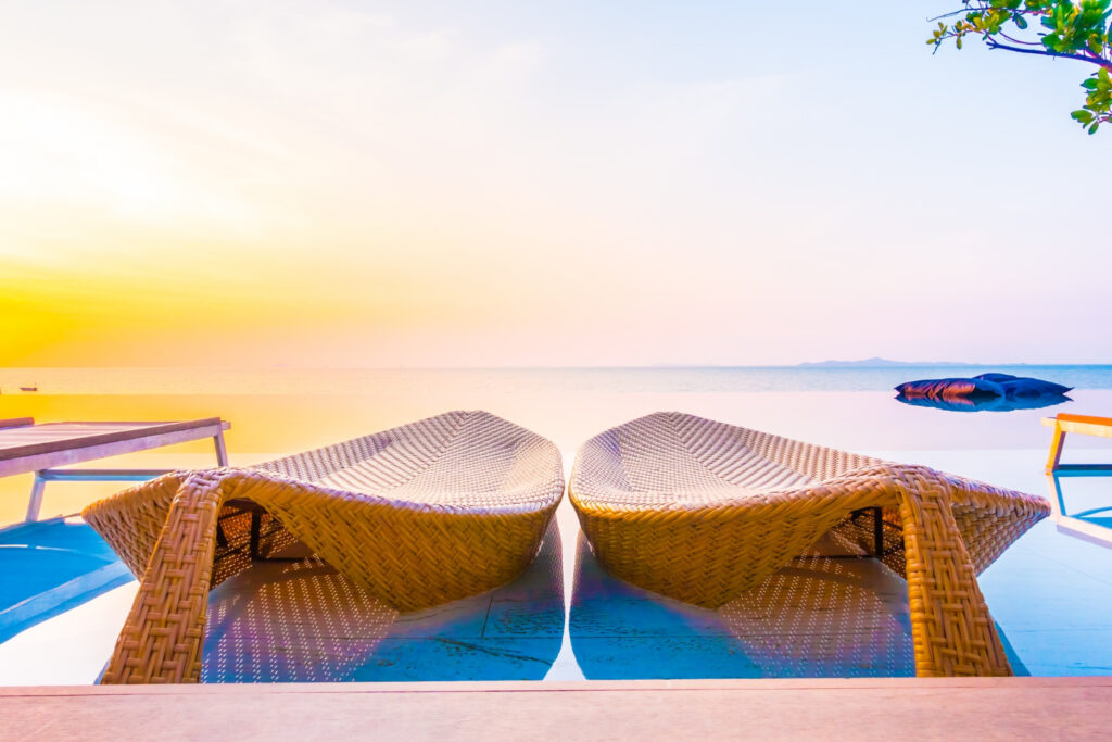 Dua kursi santai anyaman di tepi kolam renang infinity yang melambangkan ketenangan dalam layanan perjalanan privat.