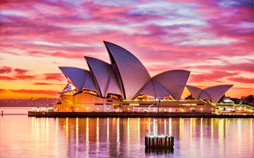 Keindahan arsitektur Sydney Opera House dengan latar belakang langit senja berwarna merah muda dan ungu yang dramatis, mencerminkan sisi romantis perjalanan musim dingin.