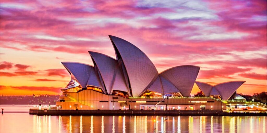 Keindahan arsitektur Sydney Opera House dengan latar belakang langit senja berwarna merah muda dan ungu yang dramatis, mencerminkan sisi romantis perjalanan musim dingin.