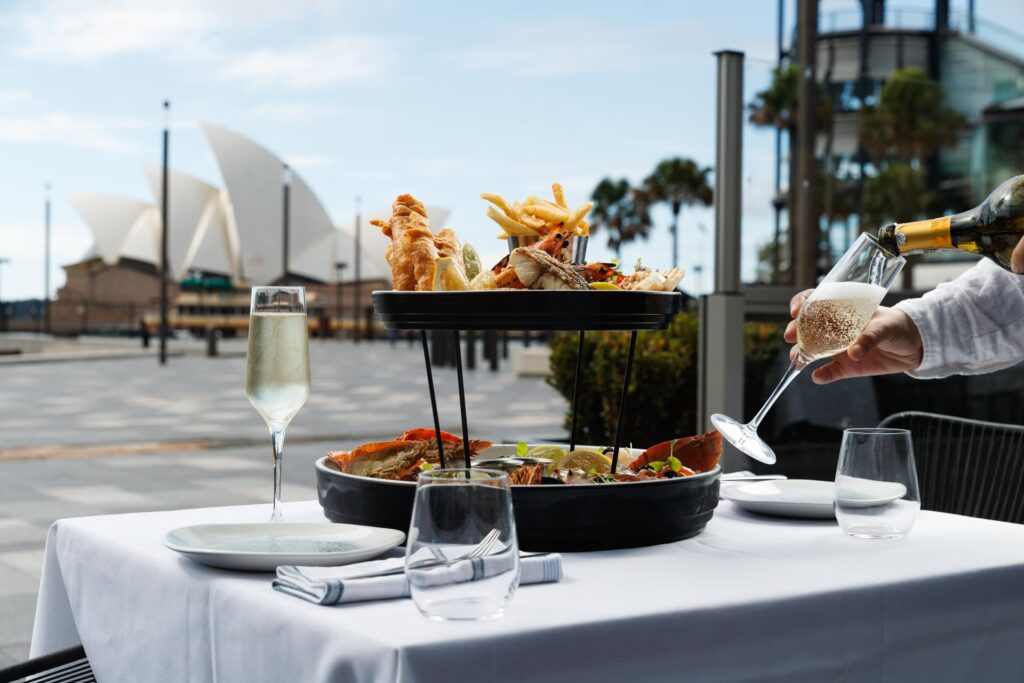 Sajian seafood mewah dan sampanye di restoran tepi laut dengan pemandangan Sydney Opera House, pengalaman kuliner bersama triplelines private trip luxury australia.