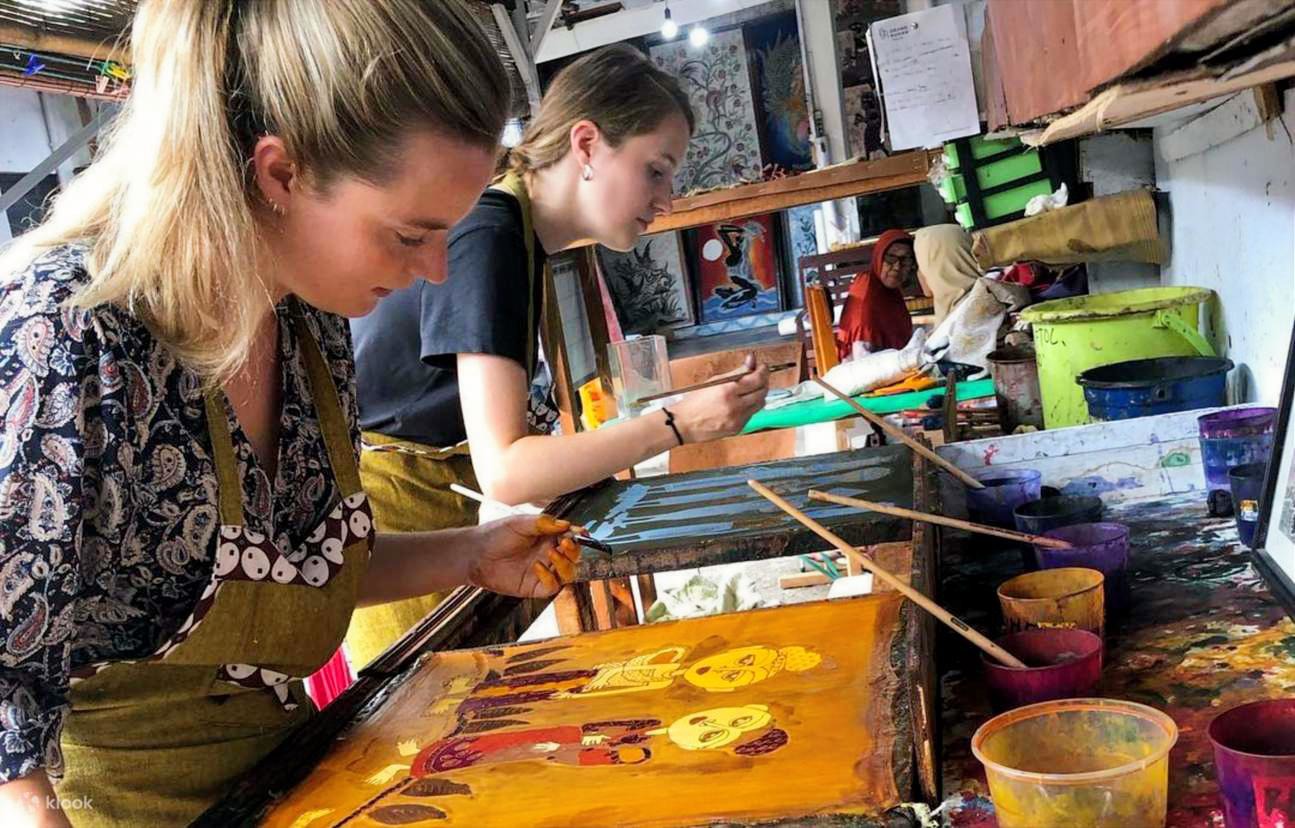 Two travelers carefully applying vibrant dyes to traditional fabric during an immersive batik painting workshop, capturing the creative Echoes of Java Journey.