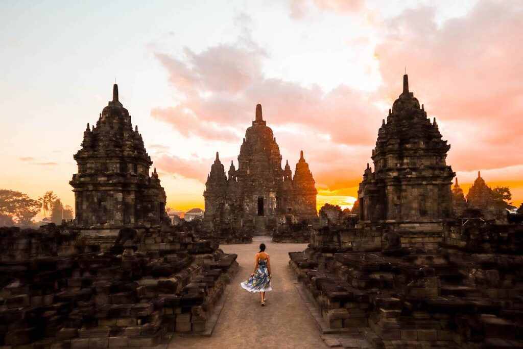 A woman walks toward the majestic Candi Sewu at sunset, surrounded by ancient stone silhouettes and the golden Echoes of Java Journey.
