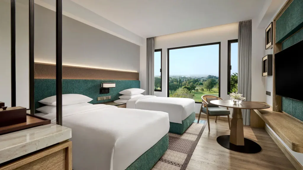 A modern premier twin room with large windows overlooking a green golf course, offering a peaceful sanctuary within the Echoes of Java Journey.