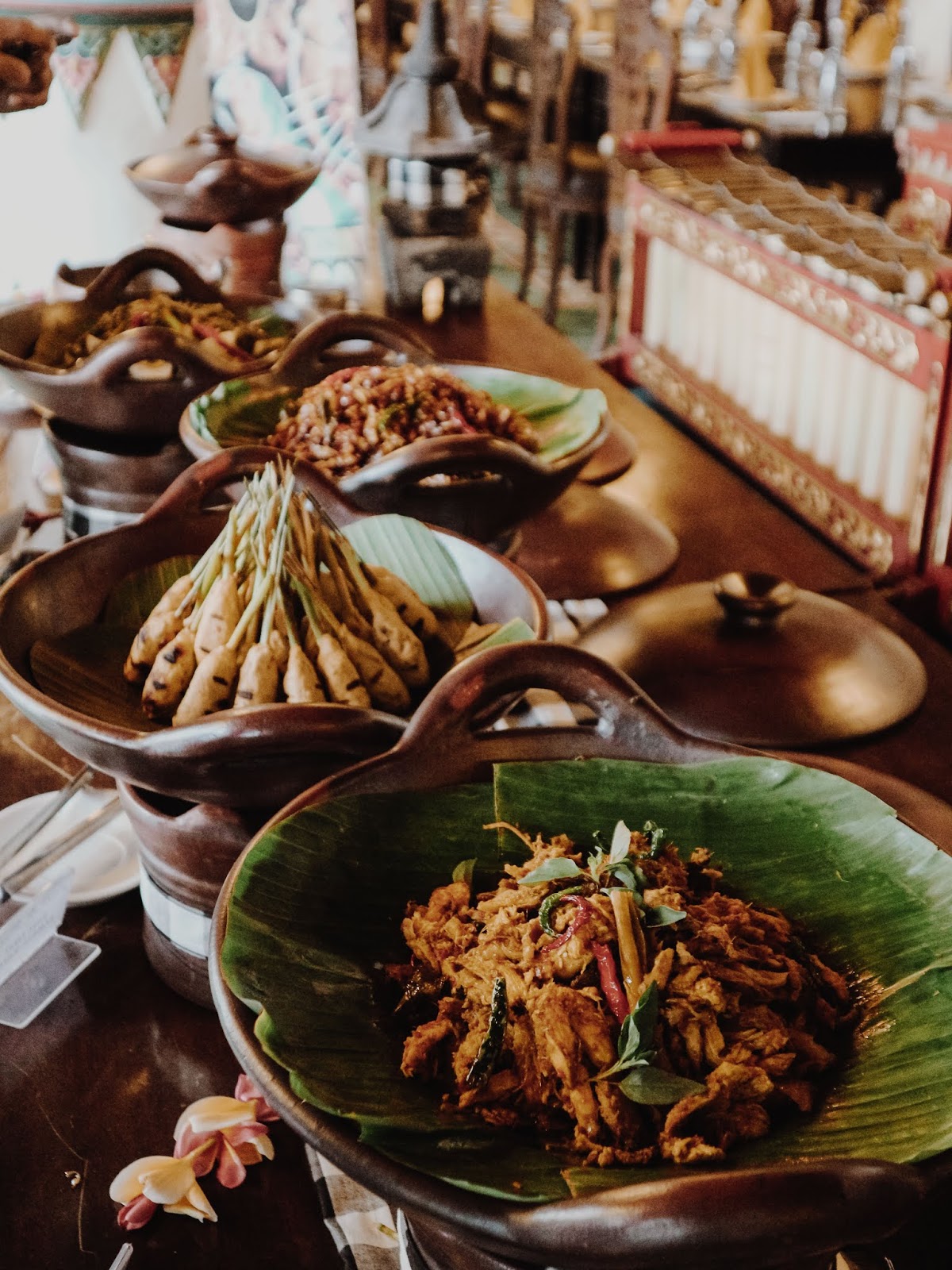 A close-up of various traditional Javanese dishes, including Sate Lilit and spicy shredded chicken, served in clay bowls lined with banana leaves.