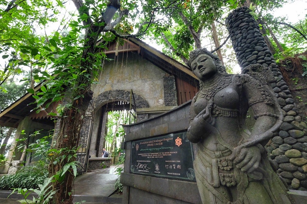 A stone statue of a Javanese figure surrounded by lush greenery and stone walls at the Ullen Sentalu Museum in Kaliurang.