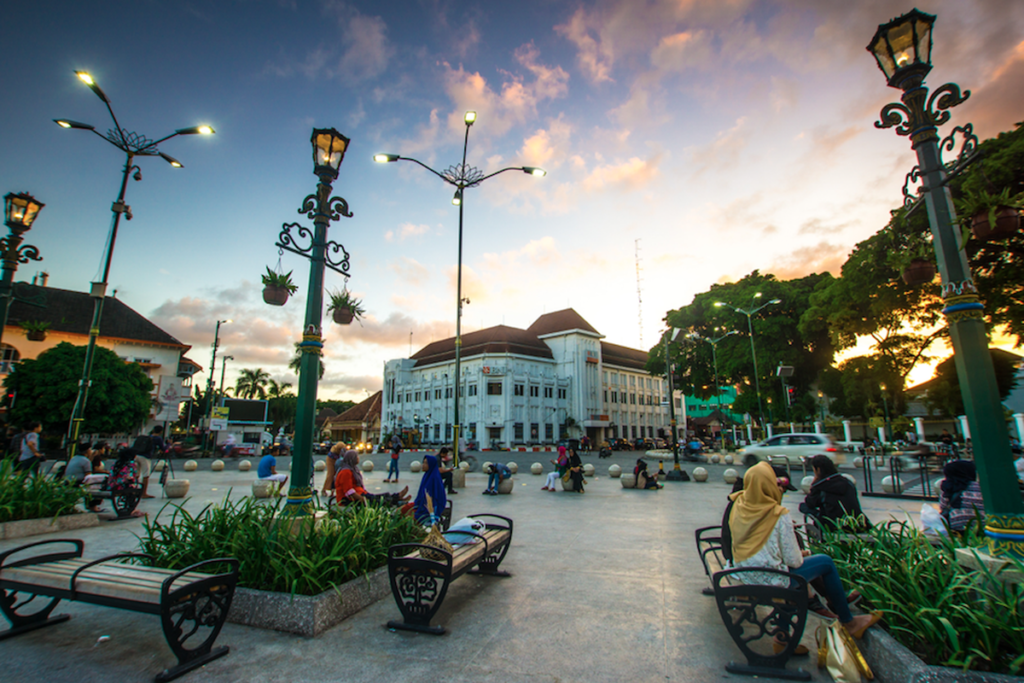 point.jpg A wide shot of the Zero Kilometer Point in Yogyakarta at sunset, featuring ornate green street lamps, people relaxing on benches, and the historic Bank Indonesia building in the background.
